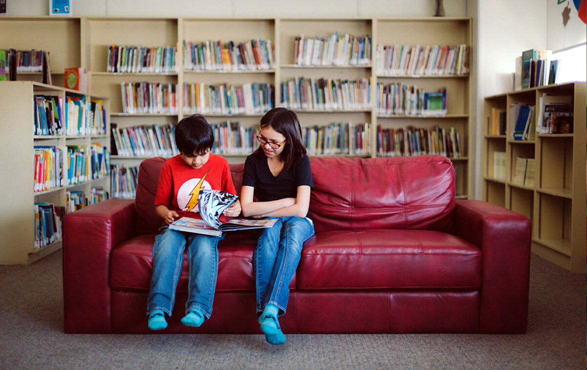 A photo of Chase and Nadine sitting on a couch reading in the library.