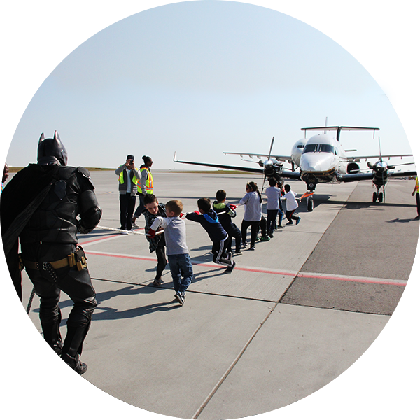 A small plane being pulled by kids and Batman.