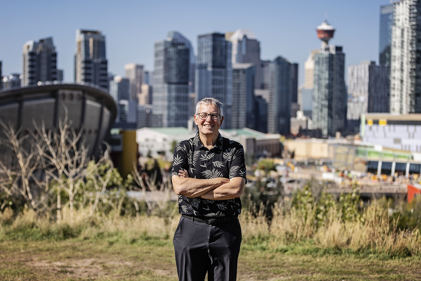 Phil Welch smiling on a grassy hill with the Calgary skyline behind him.