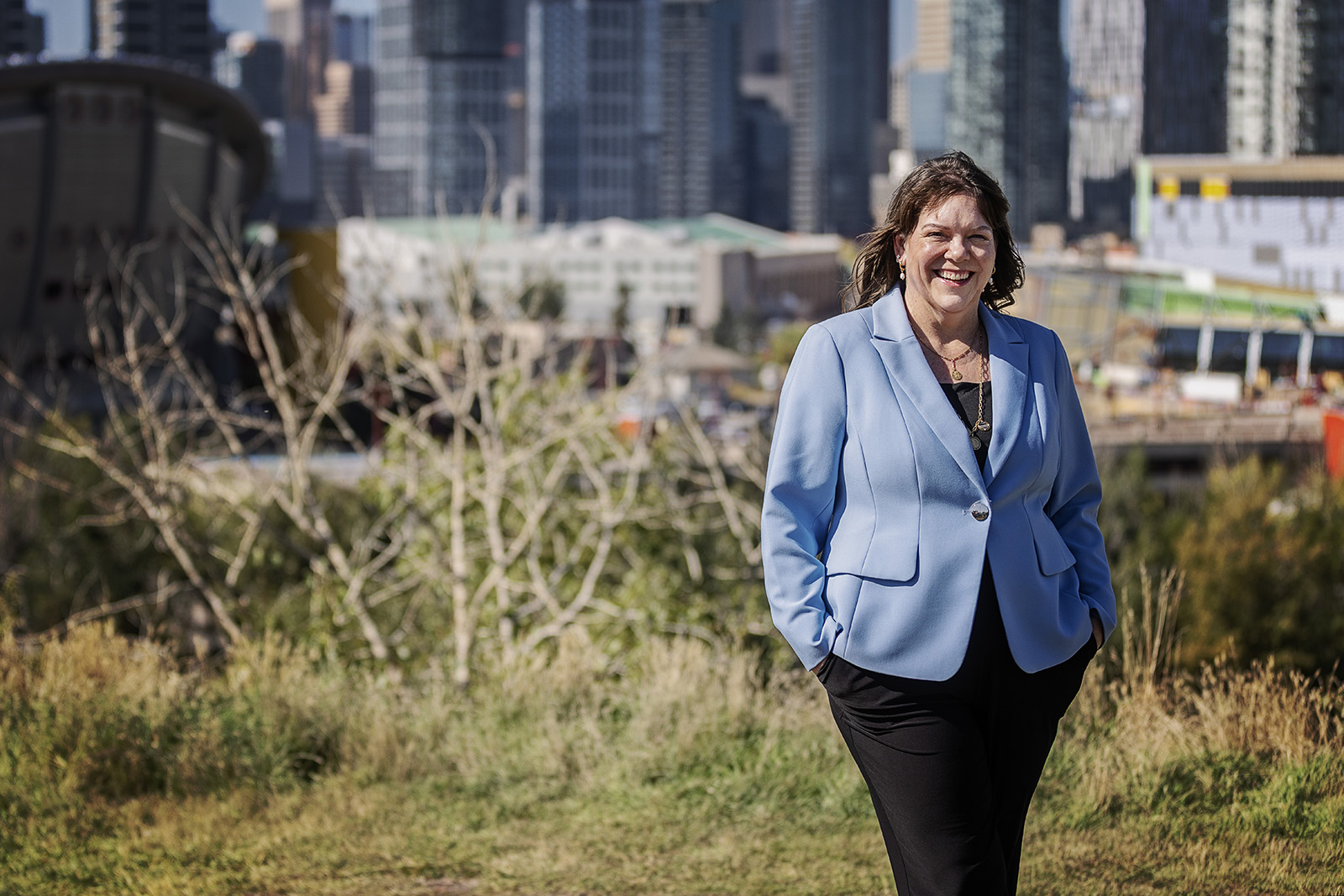 Janet Drage smiling outdoors in a light blue blazer with the Calgary skyline behind her.